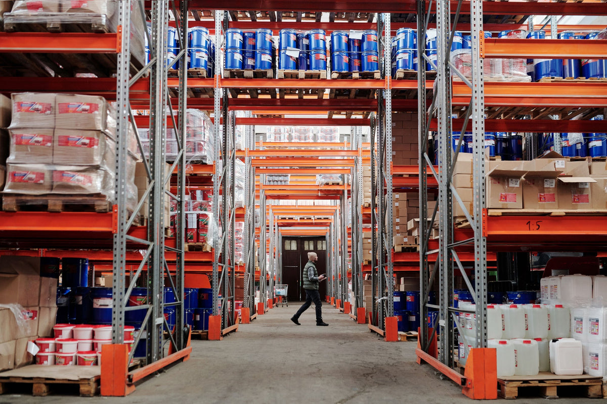 Worker walking through a large warehouse aisle with tall storage shelves